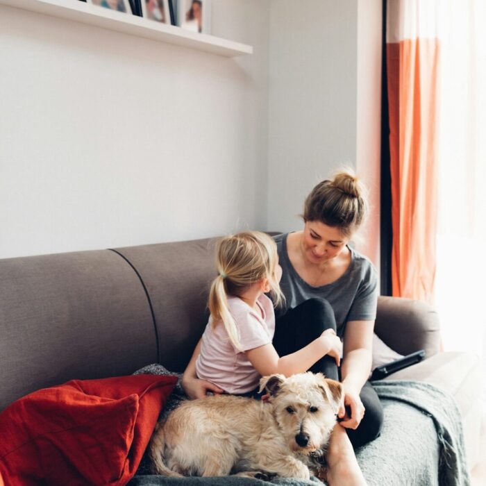 A mom, daughter, and cute dog sit on a couch,